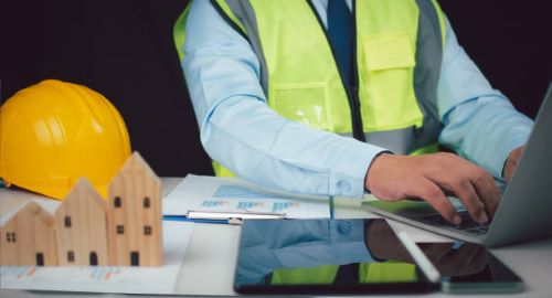 مهندس يجلس على مكتب ويستخدم لابتوب لإنجاز أعمال متعلقة ب إصدار رخصة ترميم بالرياض